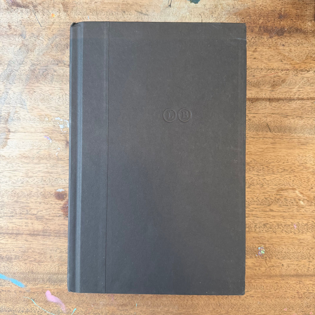 A closed black leather notebook or journal with a debossed double-circle logo on the cover, resting on a wooden tabletop.