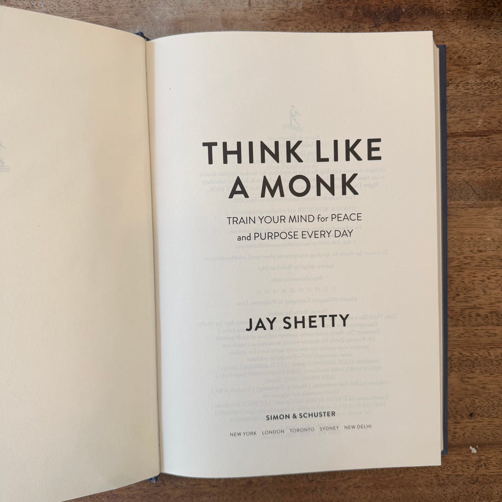 An open book titled 'Think Like a Monk' by Jay Shetty, showing the title page on a wooden surface.
